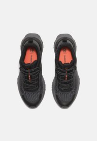 Černé sportovní boty s vrchní částí z prodyšné síťoviny, zaoblenou špičkou a oranžovými akcenty na stélkách. Mají černé šněrování a texturované gumové podrážky.