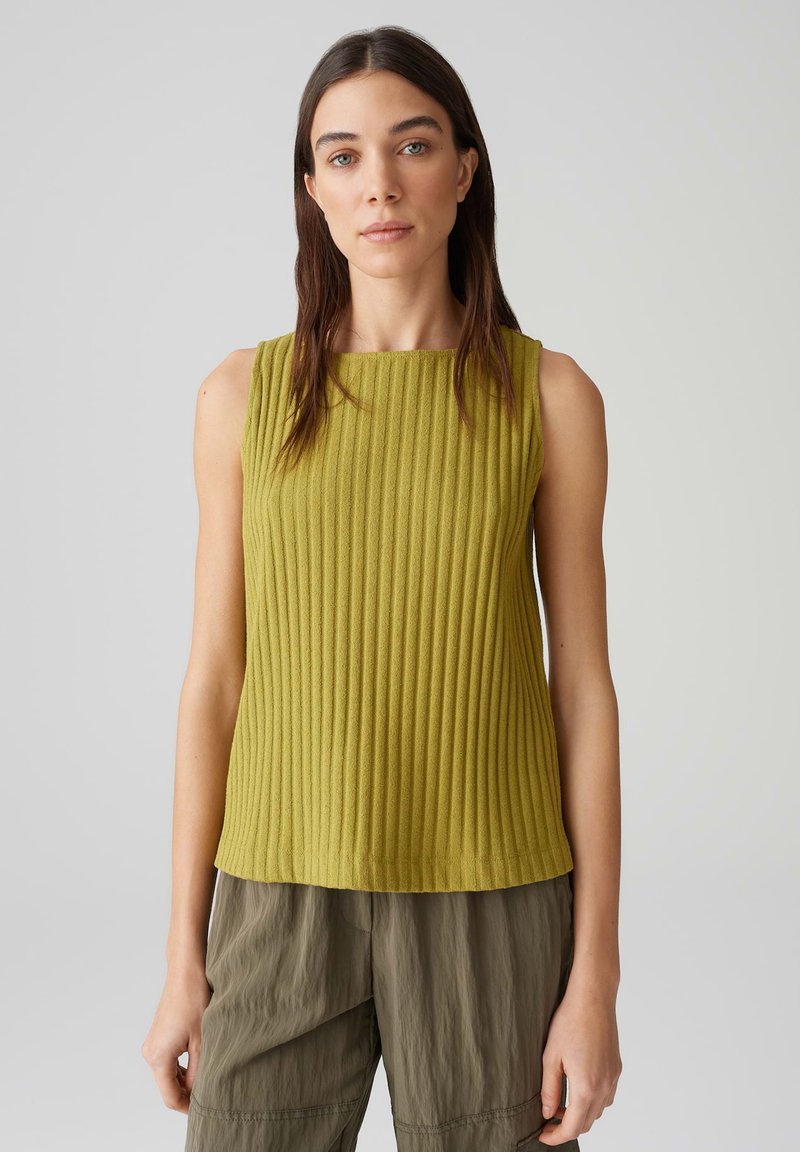 Grünes geripptes Tanktop mit Rundhalsausschnitt und ärmellosem Design, kombiniert mit lockeren, strukturierten olivfarbenen Hosen.