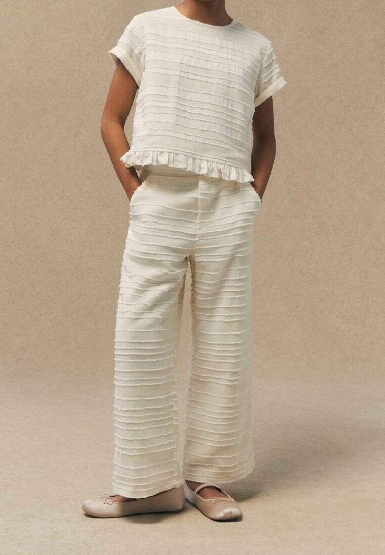 Biały, teksturowany strój w poziome paski, składający się z krótkiego topu z krótkim rękawem i luźnych spodni. Stylizowany z falbanistym wykończeniem i miękkimi balerinami.