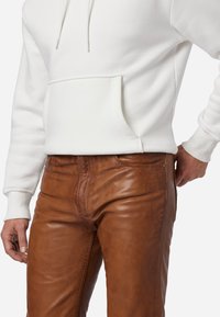 Witte sweater met koordjes en een voorzak, gecombineerd met bruine leren broek met een gladde textuur en zichtbare stikseldetails.