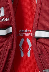 Red hiking backpack section featuring mesh paneling, reflective accents, and "deuter AIRSTRIPE" logo in silver, emphasizing ergonomic design.
