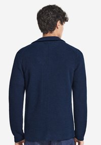 Mörkblå stickad cardigan med ett strukturerat mönster, sjalkrage och långa ärmar. Baksidan har en central söm.