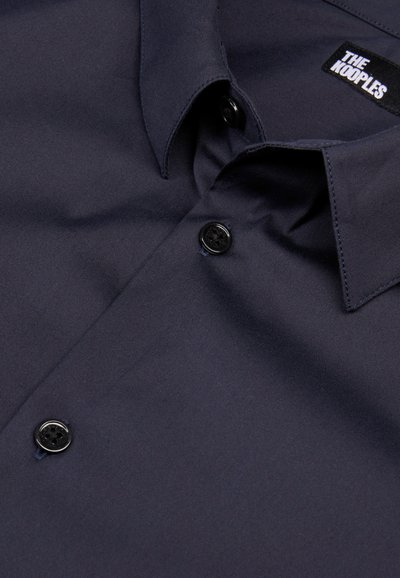 Navyblauw shirt van gladde stof met een button-down kraag, voorzien van zwarte knopen en een label met de tekst "THE KOOPLES."