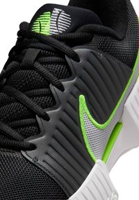 Μαύρο αθλητικό παπούτσι με υλικά από  πλέγμα και καουτσούκ. Διαθέτει γκρι επίστρωση με αυλακώσεις, λευκό και πράσινο λογότυπο ως διακριτικό και μαύρα κορδόνια.