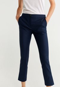 Tmavě modré kalhoty z hladké látky s přiléhavým střihem, předními kapsami a zapínáním na jeden knoflík. Zkrácená délka.