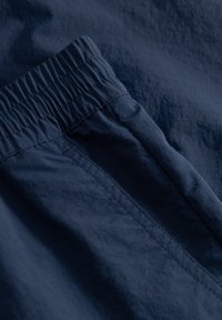 Ceinture élastique bleu marine avec une texture froncée, tissu lisse et une couture latérale. Le matériau semble léger avec un subtil éclat.