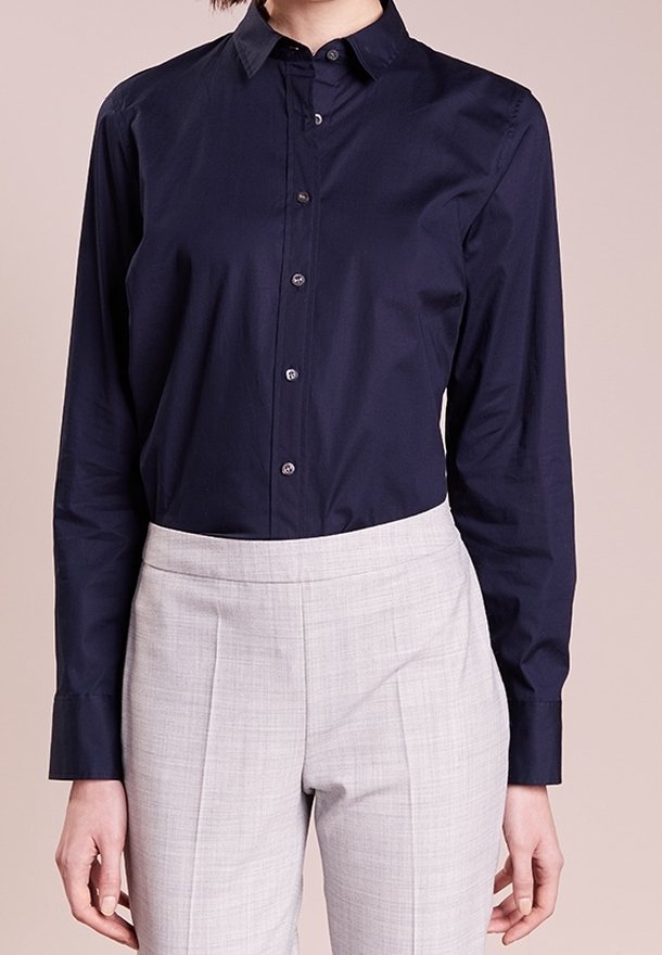 Chemise bleu marine à boutons avec manches longues, col pointu et texture lisse. Associée à un pantalon gris clair ajusté.