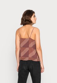 Vista traseira de uma t-shirt sem mangas, com padrão em marrom e dourado, apresentando um design floral e alças finas, combinada com jeans pretos.