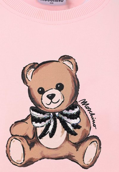 Różowy sweter z grafiką misia ozdobioną cekinowym czarno-białym krawatem. Miś ma zaokrąglony kształt i wyraźne cechy twarzy.