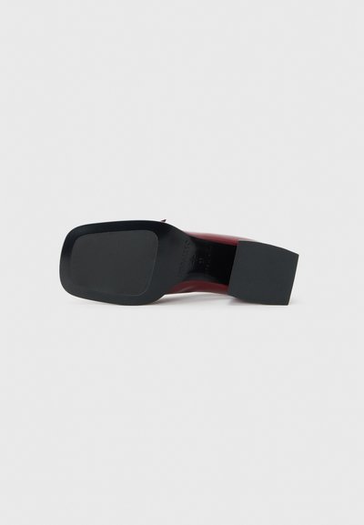 Chaussure à talon haut rouge avec une semelle noire texturée, un bout carré et un talon bloc. Surface lisse avec des accents minimaux et un design épuré.