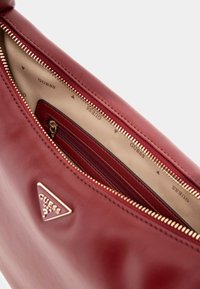 Punane nahast käekott kuldse riistvara ja lukuga, millel on kangas sisu. Sees on lukuga tasku ja nähtav brändi logo.