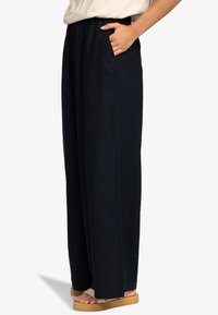 Szerokie spodnie z ciemnego dżinsu o miękkiej fakturze, z bocznymi kieszeniami i elastyczną talią dla komfortu. Casuelowy styl podkreślony prostotą.