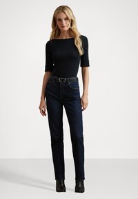 Zwarte, strakke top met driekwart mouwen en een vierkante halslijn, gedragen met hoge taille, donkerblauwe jeans, gecombineerd met een zwarte riem en enkelboots.