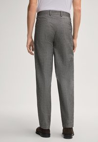 Uomo con pantaloni a quadri grigi e scarpe marroni, mostrato di spalle su uno sfondo semplice e chiaro.