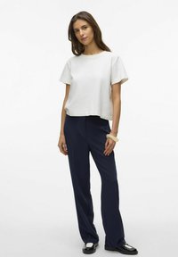 Vit kortärmad cropped t-shirt som kombineras med mörkblå randiga byxor. Modellen bär ett ljust armband och svarta skor.