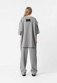 Camiseta gris de gran tamaño y pantalones a juego, hechos de tela suave. La camiseta tiene hombros caídos y un parche rectangular negro en la parte posterior.