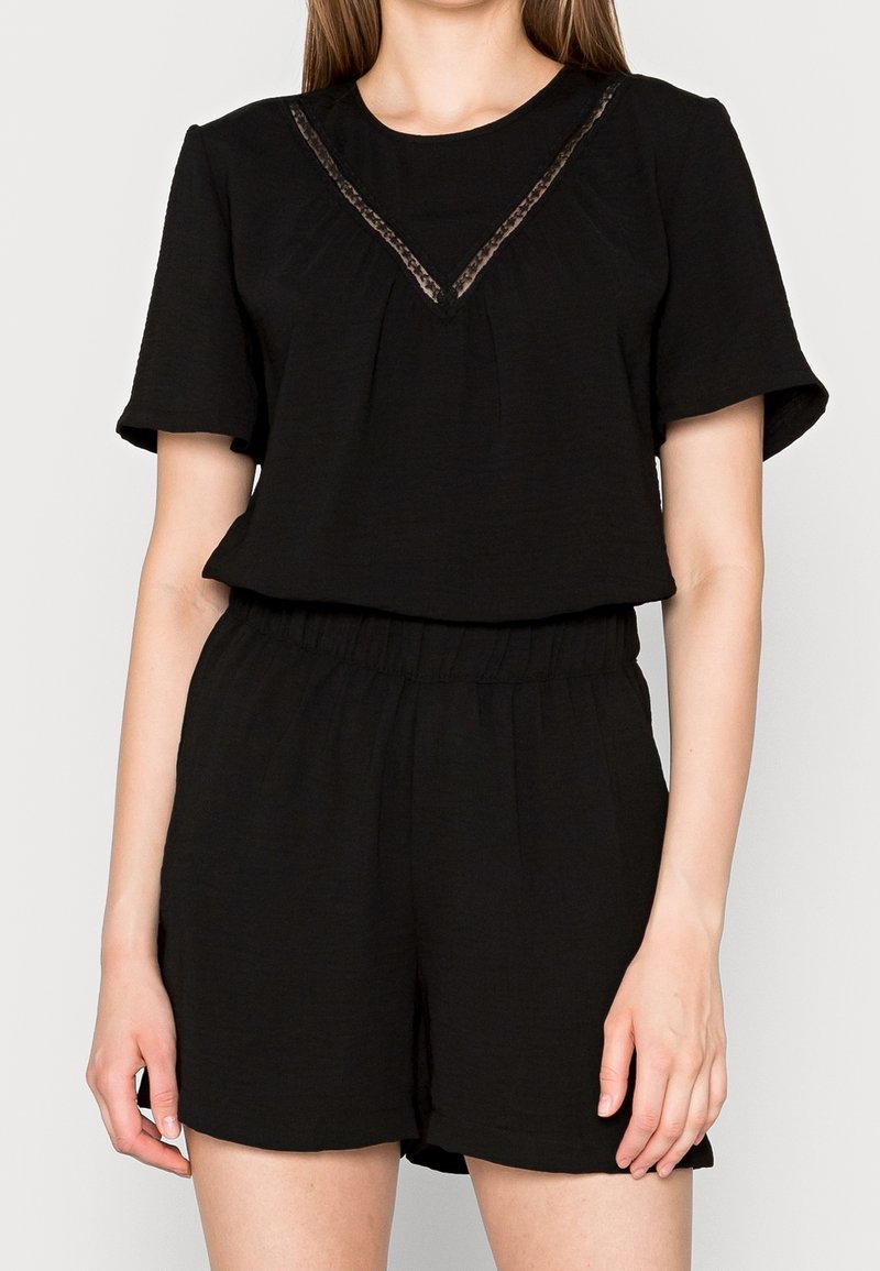 Femme portant un haut noir à manches courtes avec un détail en dentelle au niveau de l'encolure et un short noir assorti à taille élastique.
