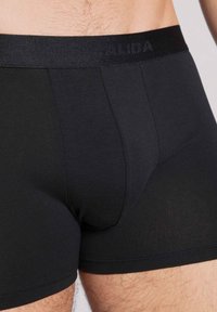 Zwarte katoenen boxershorts met een zachte, elastische tailleband waarop de merknaam staat. Zachte textuur en een aansluitend ontwerp met minimale naden.