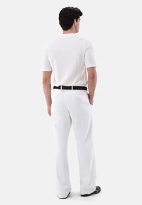 Weißes Polohemd mit kurzen Ärmeln, kombiniert mit weißen Hosen. Das Outfit weist einen dunklen Gürtel und eine glatte Textur auf, ideal für einen lässigen Look.