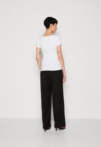 T-shirt blanc à manches courtes avec un col rond, associé à un pantalon large noir. Le tissu semble lisse et ajusté à la taille.