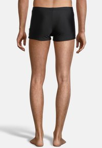 Shorts de bain noirs au design ajusté, fabriqués en matériau lisse et extensible. Dotés d'une taille sans quincaillerie visible.