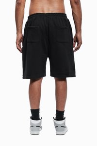 Svarte shorts med elastisk midje, to baklommer, og en løs passform, kombinert med grå og hvite joggesko og svarte sokker.