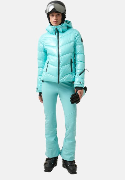 Lichtblauwe donsjas met capuchon, gecombineerd met bijpassende skibroek. Zwarte handschoenen en skischoenen maken de outfit compleet. Glad, glanzend textuur.