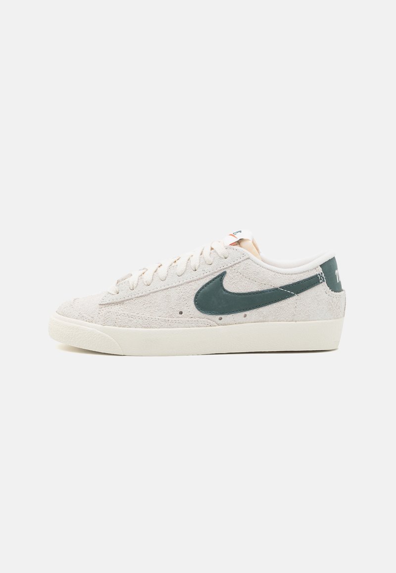 Baskets basses en daim beige avec un logo Nike vert foncé, lacets blancs et semelle en caoutchouc crème, présentées sur fond blanc uni.