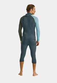 Hooded long-sleeve top and cropped leggings in teal and dark green. Smooth texture; fitted design with contrasting color sleeves.