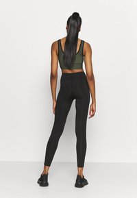 Top corto a coste verde scuro abbinato a leggings neri a vita alta. Scarpe sportive nere completano l'outfit.