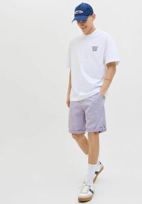 Witte katoenen t-shirt met logo, lichtpaarse shorts, witte en marineblauwe sneakers, gecombineerd met een marineblauwe pet. Casual, relaxed fit.