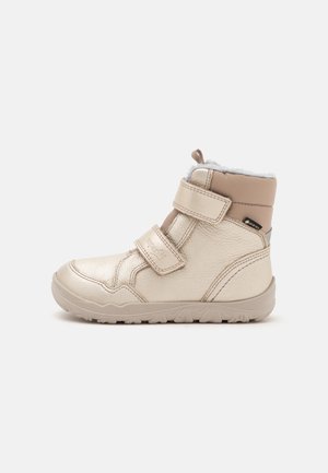 Bota de invierno beige para niños, con dos correas de velcro, suela texturizada y forro interior suave, mostrada de lado sobre un fondo liso.
