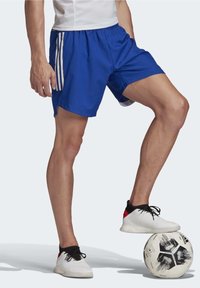 Modré sportovní šortky s elastickým páskem a bílými proužky po stranách, doplněné černo-bílými sportovními botami a fotbalovým míčem.