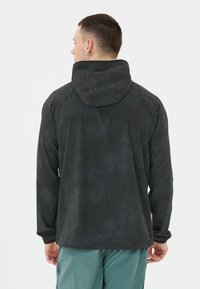 Schwarze Kapuzenjacke aus strukturiertem Stoff mit einem subtilen Muster. Lange Ärmel und elastische Bündchen. Rückansicht zeigt Details der Kapuze.