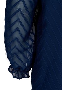 Manche bleu marine transparente avec motif texturé en zigzag et détail de poignet élastique froncé.