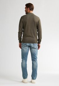 Maglione a maglia verde oliva con maniche lunghe, polsini e orlo a coste, abbinato a jeans azzurri e sneakers bianche. Viene mostrata la vista posteriore.