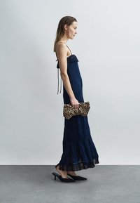 Φόρεμα σε βαθύ μπλε χρώμα με στρώσεις και φράτζες στο τελείωμα, ρυθμιζόμενους ιμάντες και υφή υφάσματος· συνδυασμένο με τσάντα φάκελο με λεοπάρ μοτίβο και μαύρες γόβες.