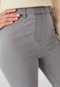 Jeans grises de tiro alto hechos de denim con una textura suave. Las características incluyen un corte ajustado, bolsillo lateral y detalles de costura.
