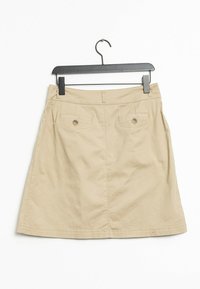 Beige bomullkjol med en utsvängd design, med två bakfickor med knappstängning och en slät textur. Hänger från en svart krok.