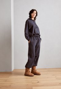 Ciemnoszara bluza z kapturem i sznurkiem, dopasowane luźne spodnie oraz jasnobrązowe zamszowe botki. Gładka tkanina i swobodny design.