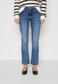 Blå denimjeans med rett snitt, fem lommer og subtil falming. Kombinert med en svart og hvit stripete genser og svarte leiligheter.