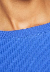 Ribbad blå topp med vid halsringning, med subtila sömnadsdetaljer och en slät yta som framhäver materialets stretchighet.