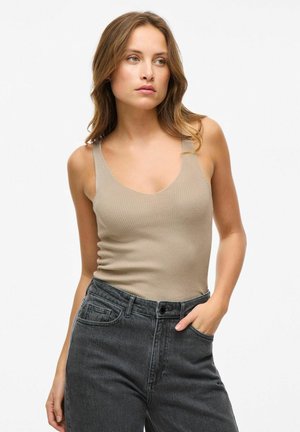 Top de tirantes de canalé beige con tirantes anchos, con un escote en V. Combinado con unos vaqueros de mezclilla oscuros de tiro alto.