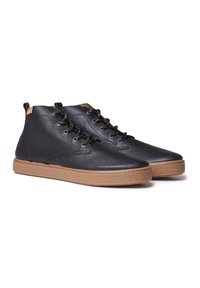 Botas de tobillo de cuero negro con superficie texturizada, diseño de cordones y suela de goma marrón. Cuenta con ojales de metal y una pestaña en el talón trasero.