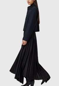 Granatowa krótka kurtka z wysokim kołnierzem, z zapięciem na guziki oraz dekoracyjnym sznurowaniem, w zestawieniu z długą, plisowaną czarną spódnicą i kozakami do kolan.