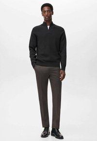 Maglione nero con zip, pantaloni grigi su misura, scarpe nere stringate. Tessuto liscio, design aderente, texture sottile nel maglione e dettagli delle pieghe nei pantaloni.