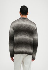 Sweter dziergany w odcieniach szarości z gradientowym wzorem, wyposażony w okrągły dekolt, ściągacze przy mankietach oraz luźny krój. Miękka tekstura.