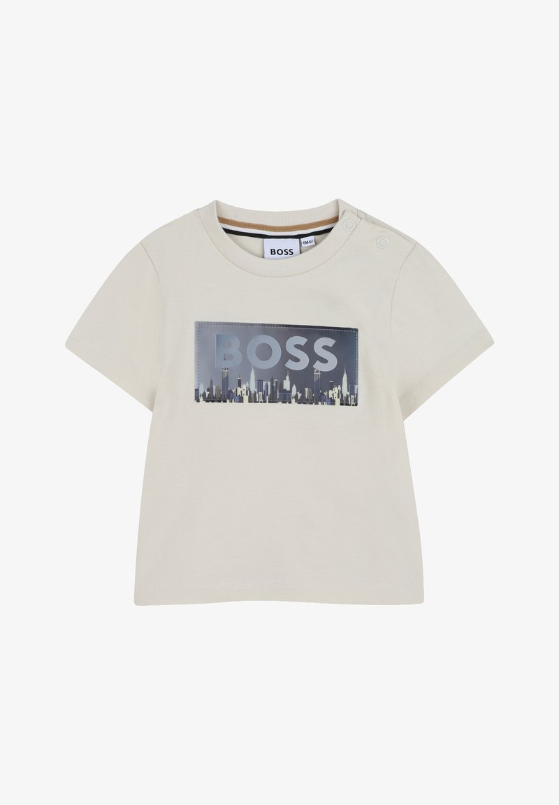 Chemise pour bébé à manches courtes beige avec texte "BOSS" et graphique de skyline de la ville sur le devant, boutons-pression sur l'épaule gauche.