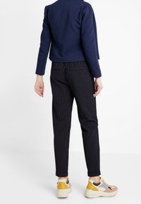 Merinovärinen texturerad kavaj i kombination med svarta randiga byxor och flerfärgade sneakers. Klädesplaggen har en avslappnad passform och skräddarsydd design.