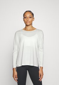 White long-sleeve top with a round neckline and dropped shoulders, featuring a loose fit and side slits, made from a lightweight fabric.